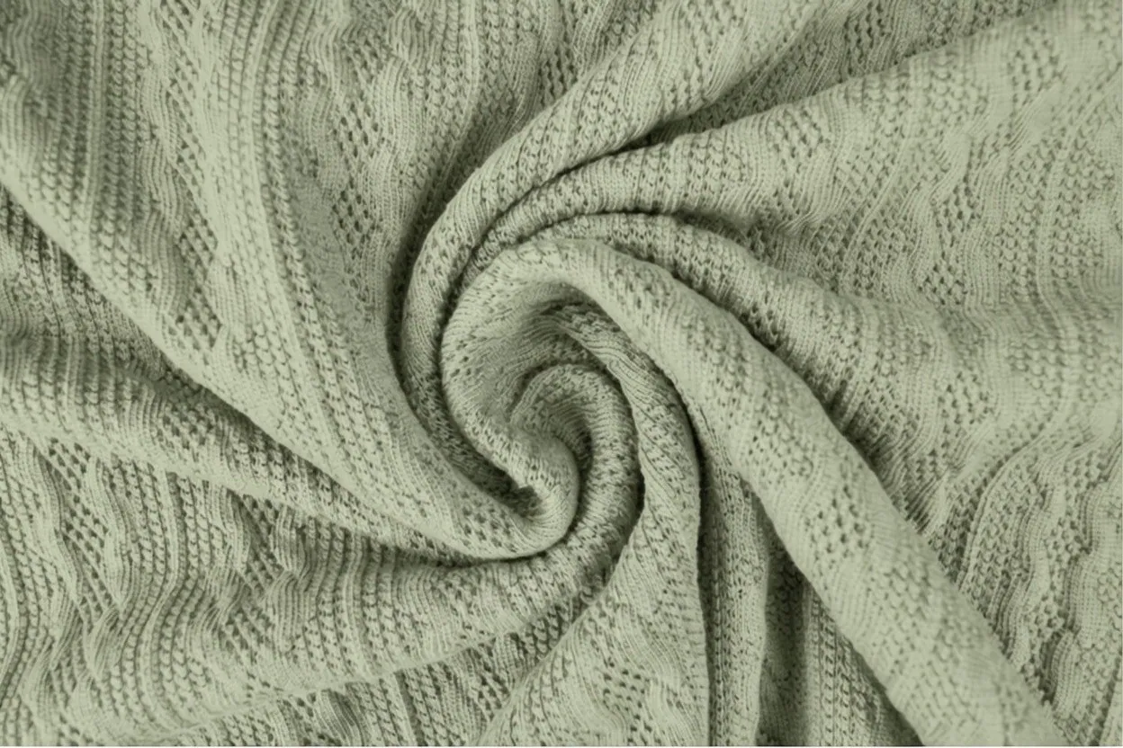 Jacquard knit fabric in soft sage cotton with intricate woven-in geometric pattern, manufactured at Apex Corporation knitwear factory in Karachi Pakistan